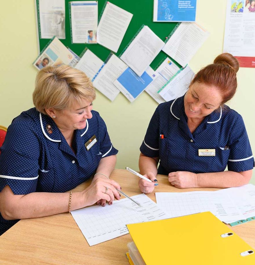 Two members of staff smiling whilst they take notes together.