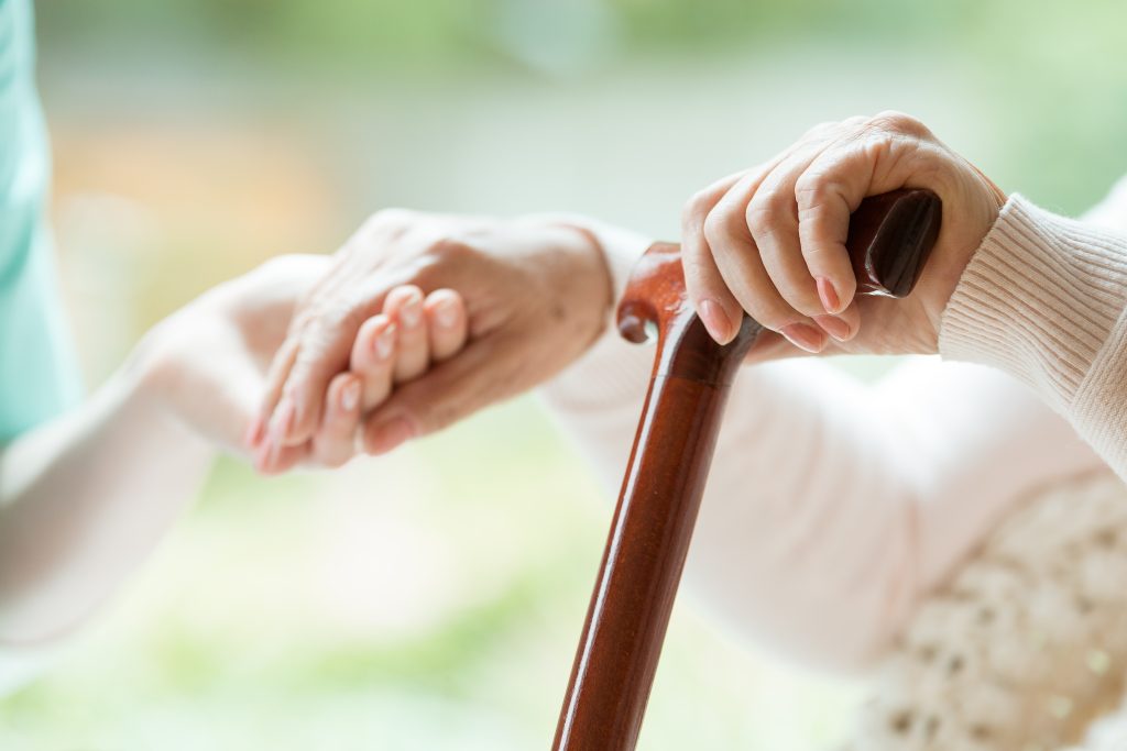 An up close shot of the hand of an elderly resident on their walking stick with their other hand in the hand of someone else.