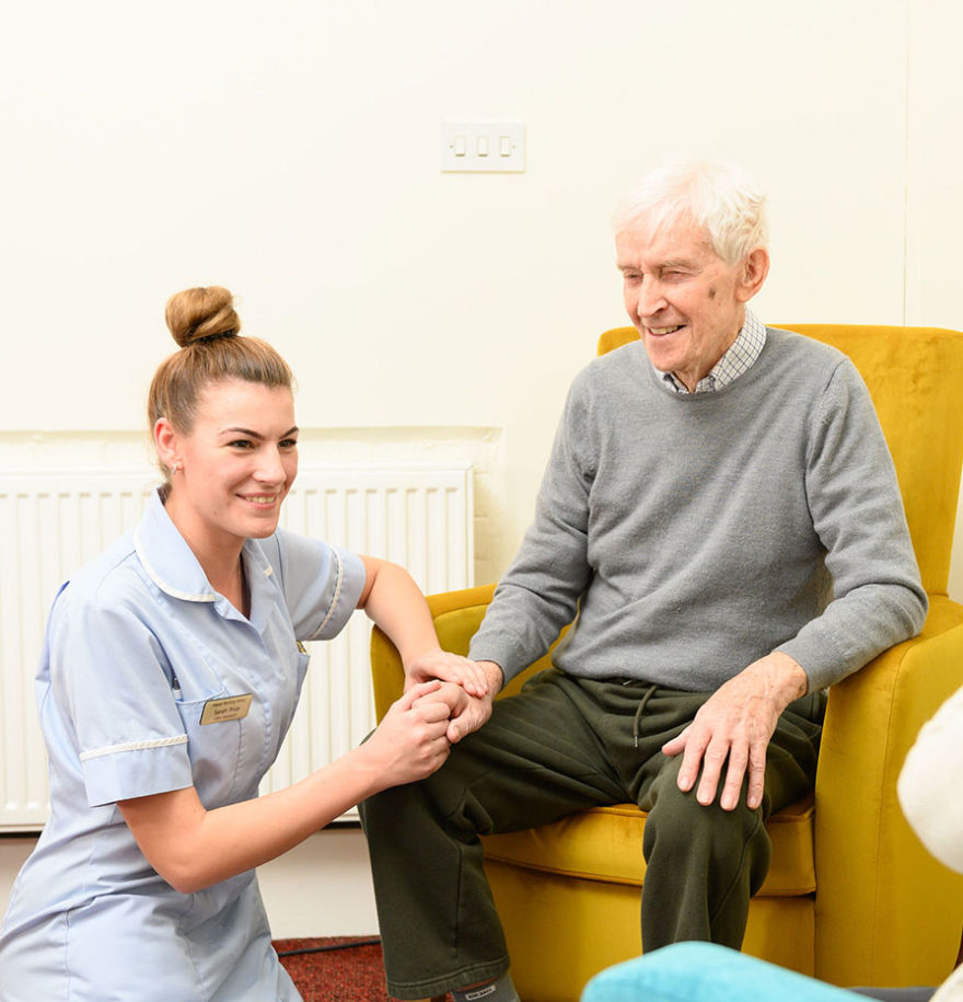An elderly resident and member of staff holding hands and smiling.