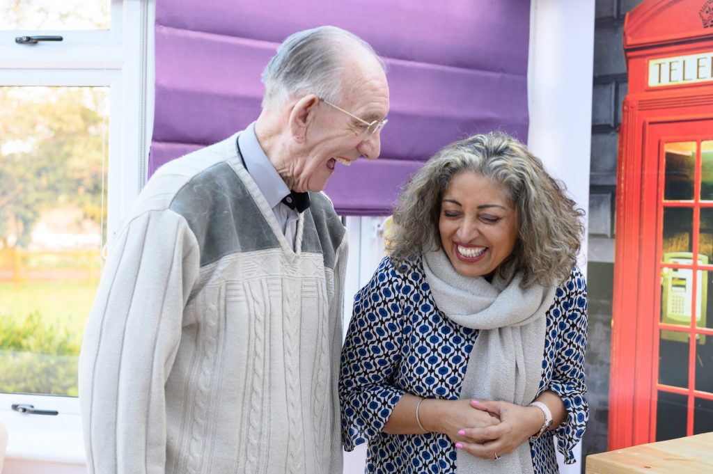 A middle aged woman and elderly resident laughing beside one another.