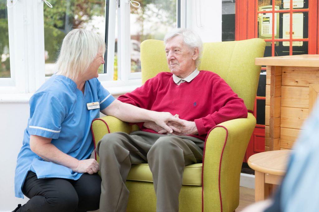 Care worker resting their hand on the hand of an elderly resident.